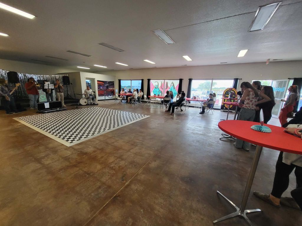 Spacious venue with a dance floor, a red table, and people mingling near windows.