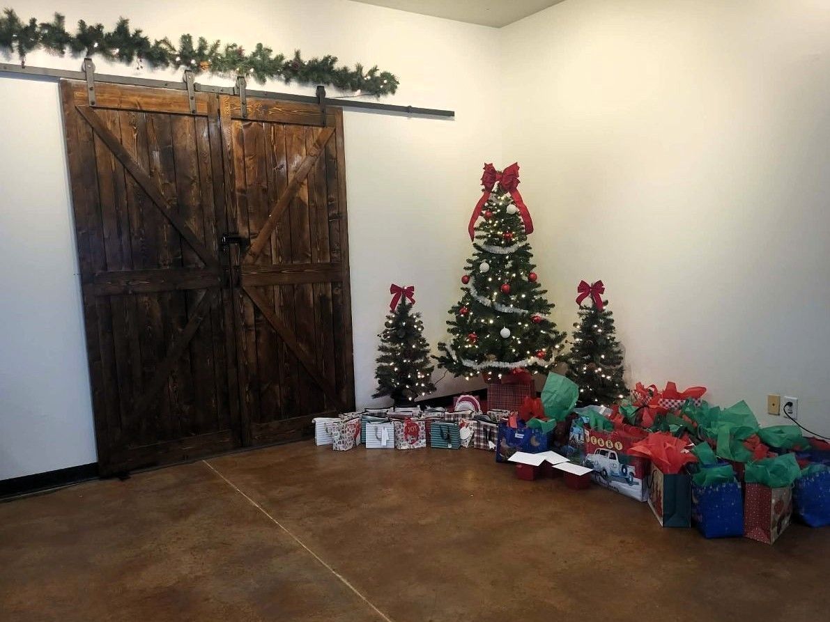 Christmas decorations: trees, presents, and a barn door in a room with a brown floor and white walls.