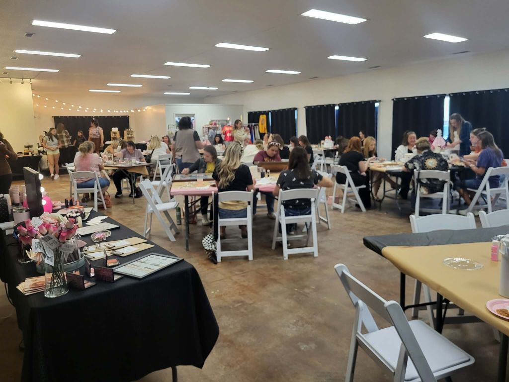 Craft fair in a large room with tables, vendors, and attendees browsing and interacting.