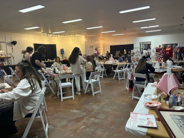 A well-lit event rental space with people at tables, some standing. Vendors, possibly a craft fair, with displayed items.