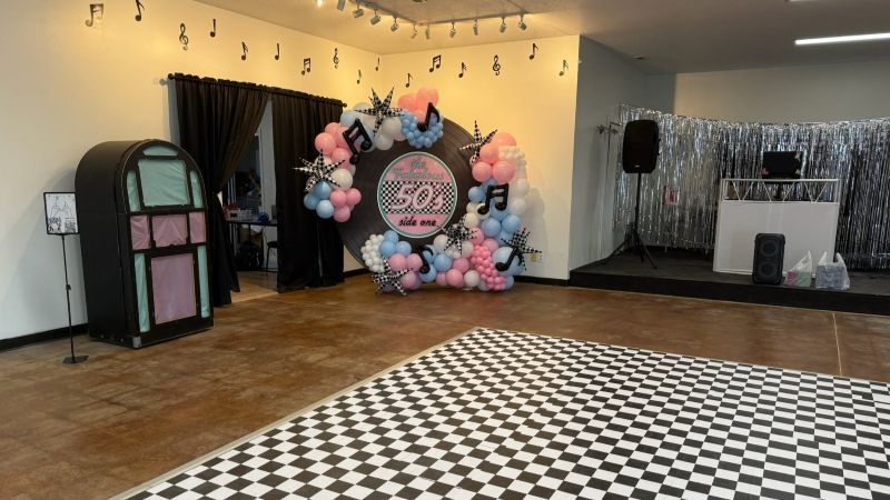 A 1950s themed party room with a jukebox, checkered dance floor, and balloon arch.