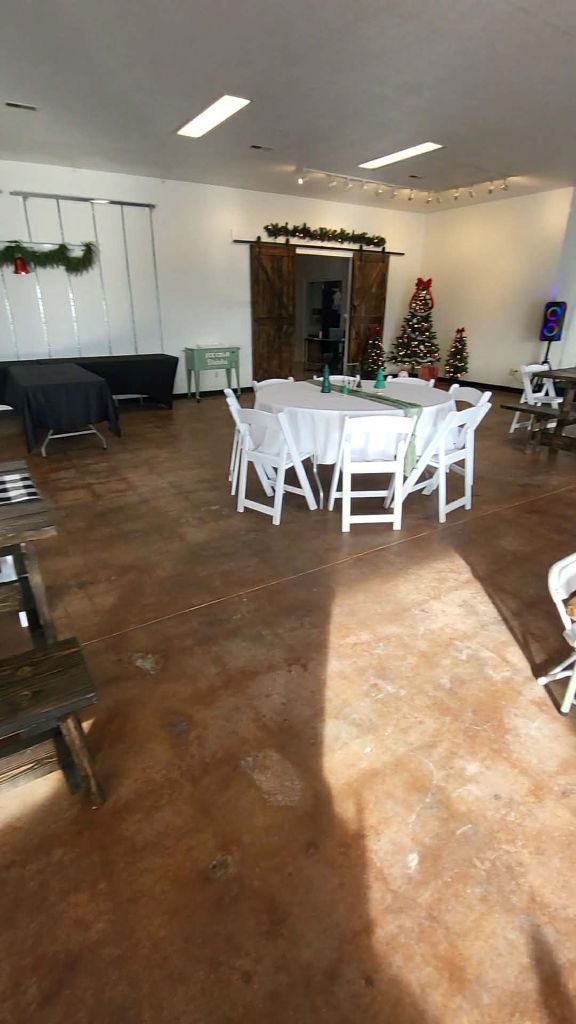 Empty event space, stained concrete floor, round table set for guests, Christmas decorations.