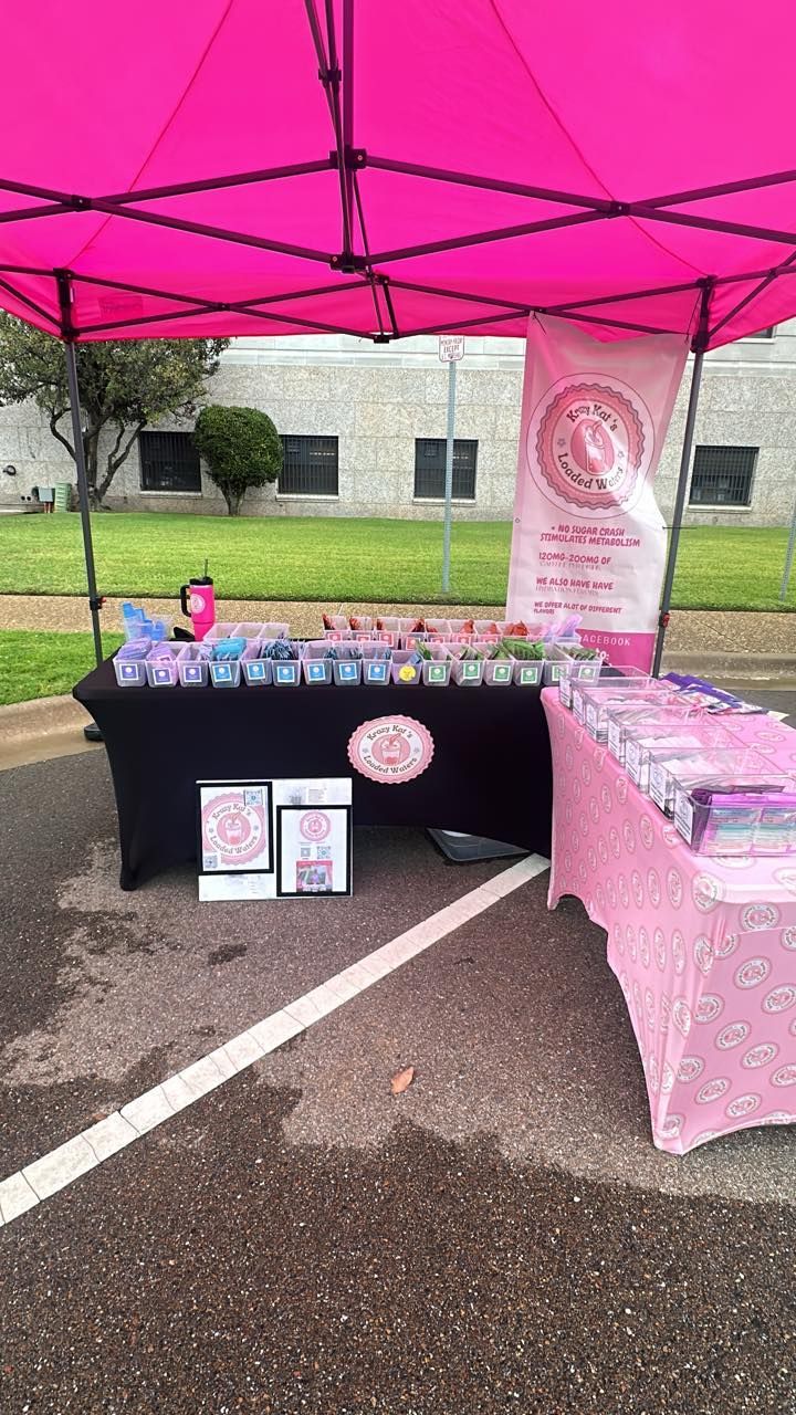 Pink vendor booth at an outdoor event. Products on display under a pink tent.
