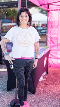 A vendor's table displays crafts, with a pink sign, indoors.