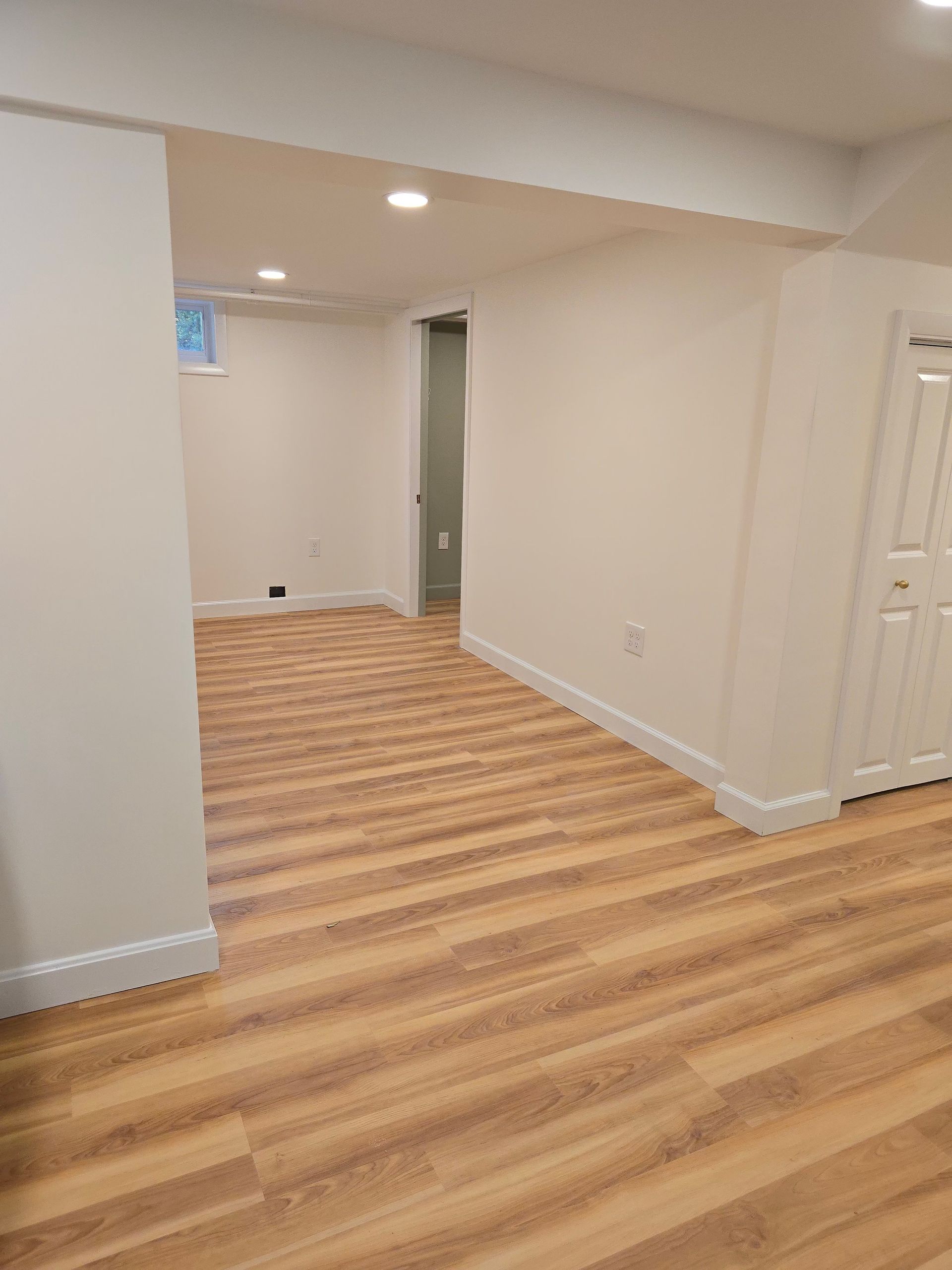 Finished basement living area with new wood-look flooring and recessed lighting.