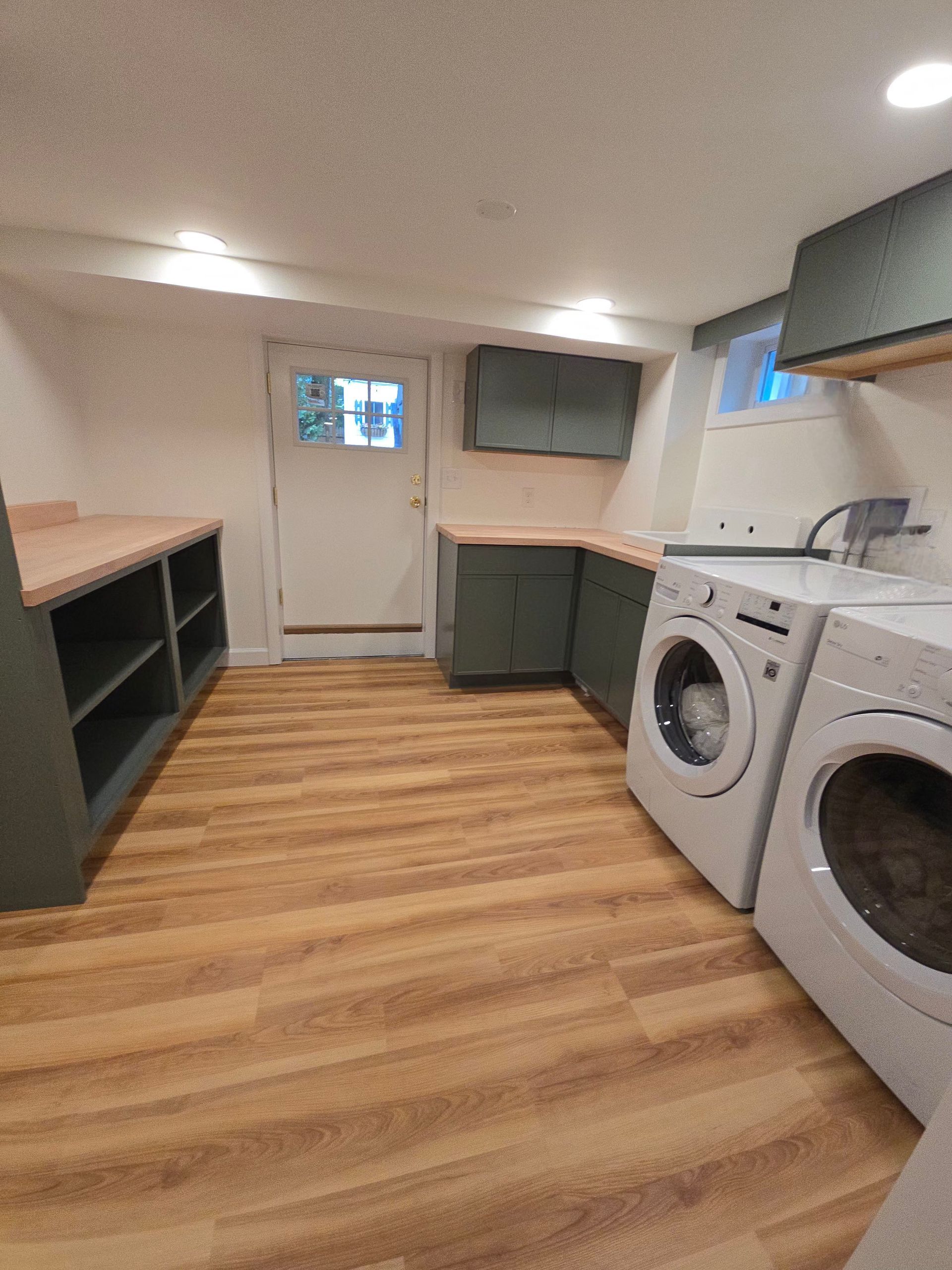 Finished basement laundry room with sage green cabinets and butcher block counters.