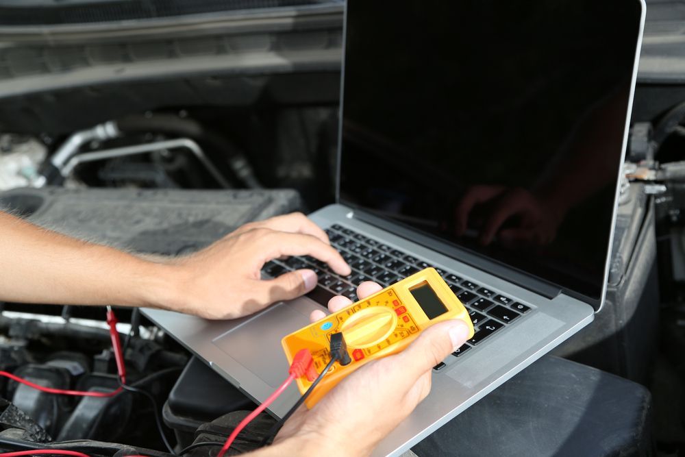 Person Using Laptop and Multimeter in a Car Engine Bay — Calvin's Mobile Mechanics In Upper Coomera, QLD