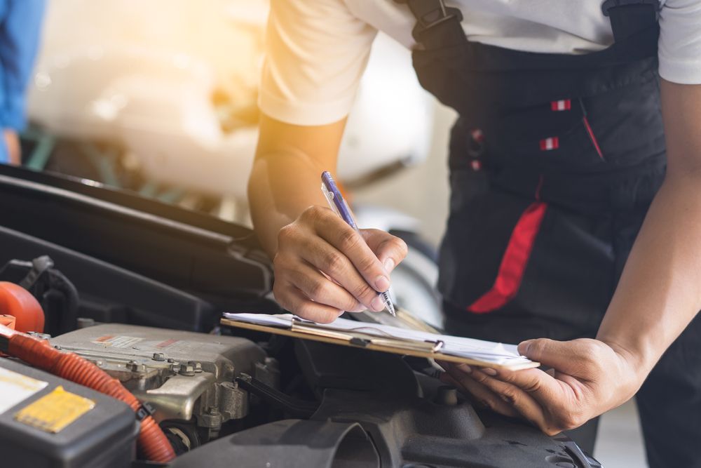 Mechanic Writing on Clipboard While Inspecting a Car Engine — Calvin's Mobile Mechanics In Helensvale, QLD