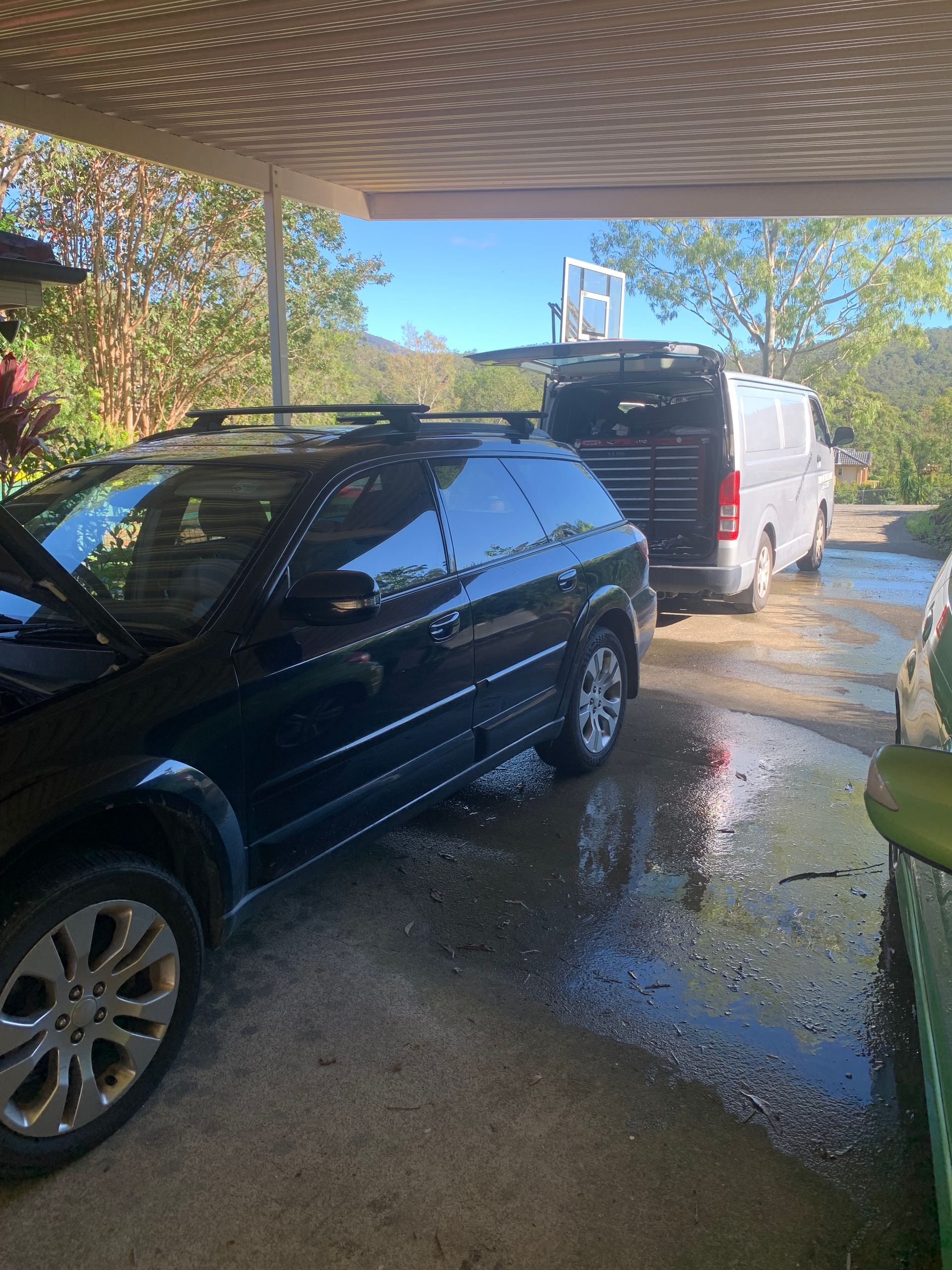 Black car and white van parked under a carport, on a wet concrete surface — Calvin's Mobile Mechanics In Elanora, QLD