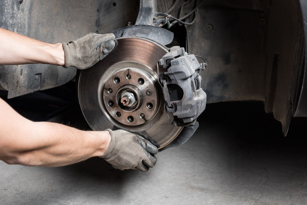 Hands With Work Gloves Removing a Car Brake Rotor in a Garage — Calvin's Mobile Mechanics In Helensvale, QLD
