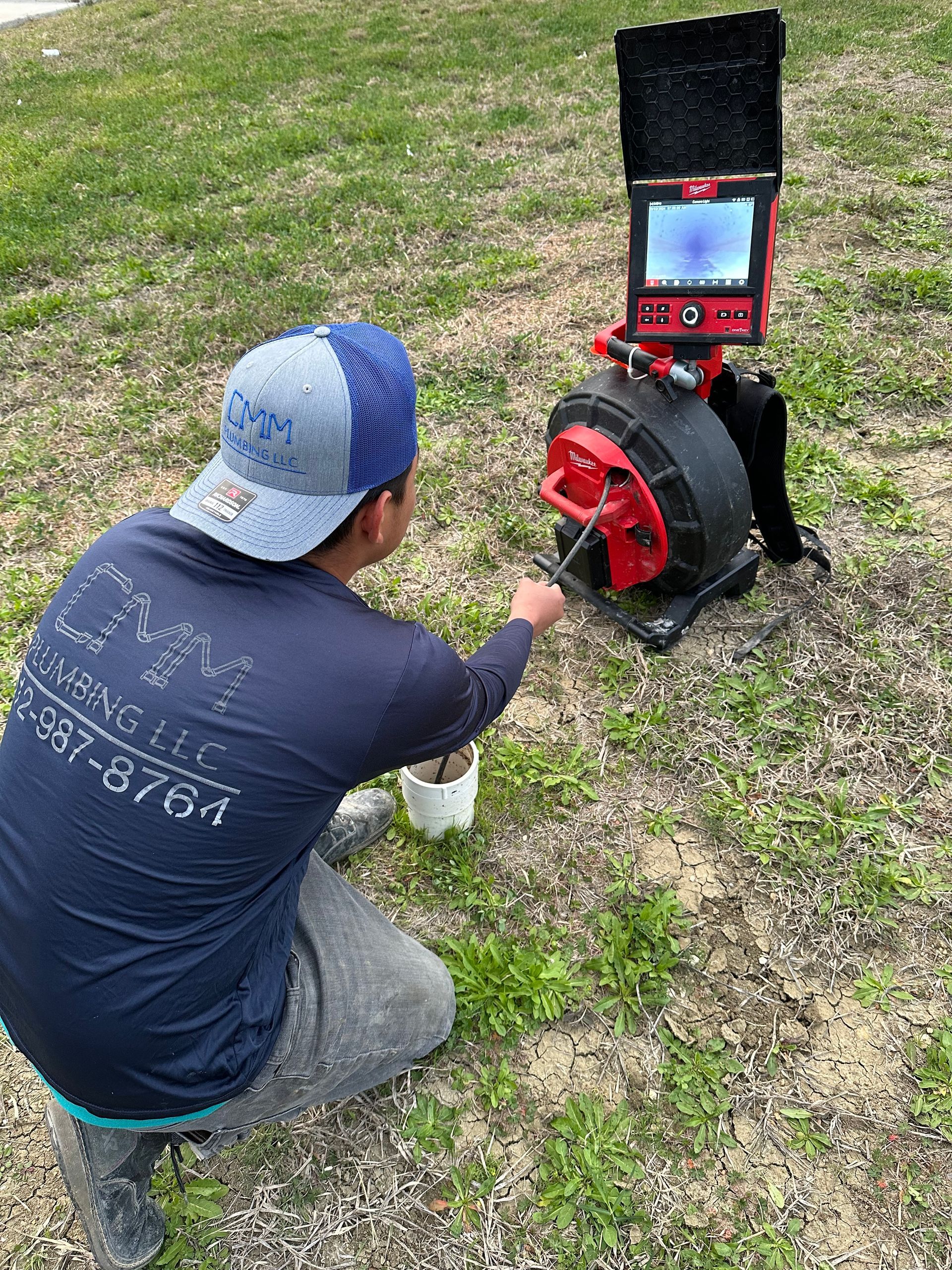 a man is kneeling down in front of a drain camera .