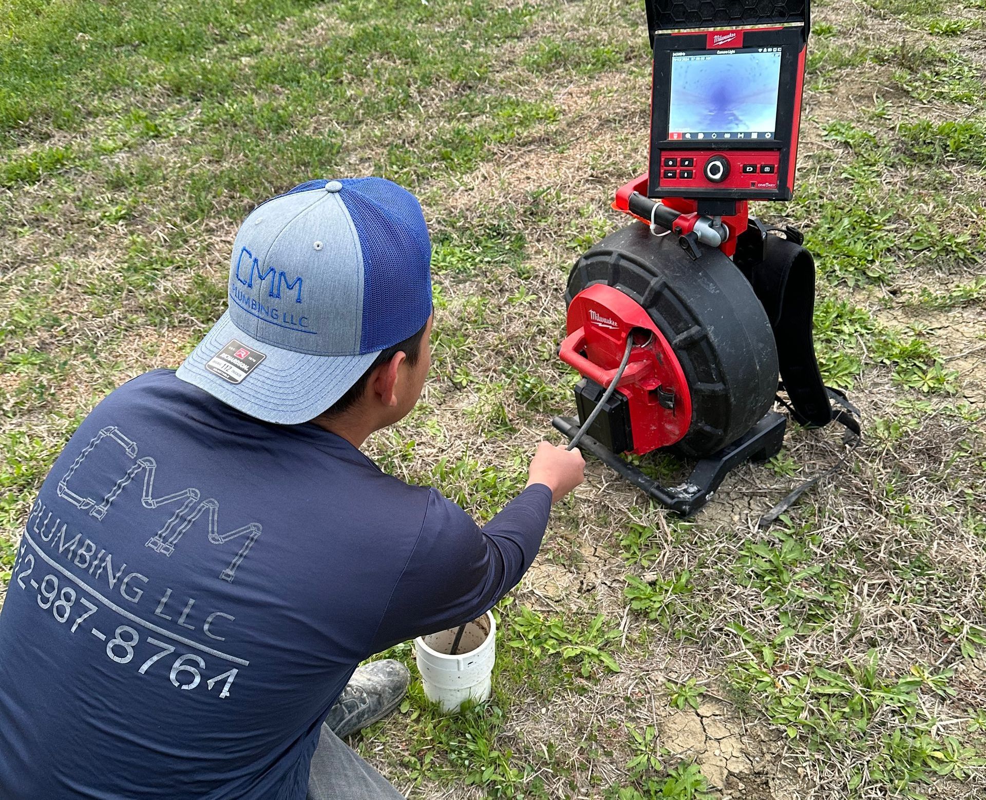 a man is kneeling down in front of a drain camera .