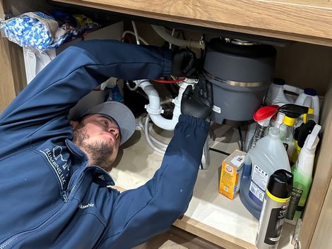 a man is fixing a garbage disposal under a sink .