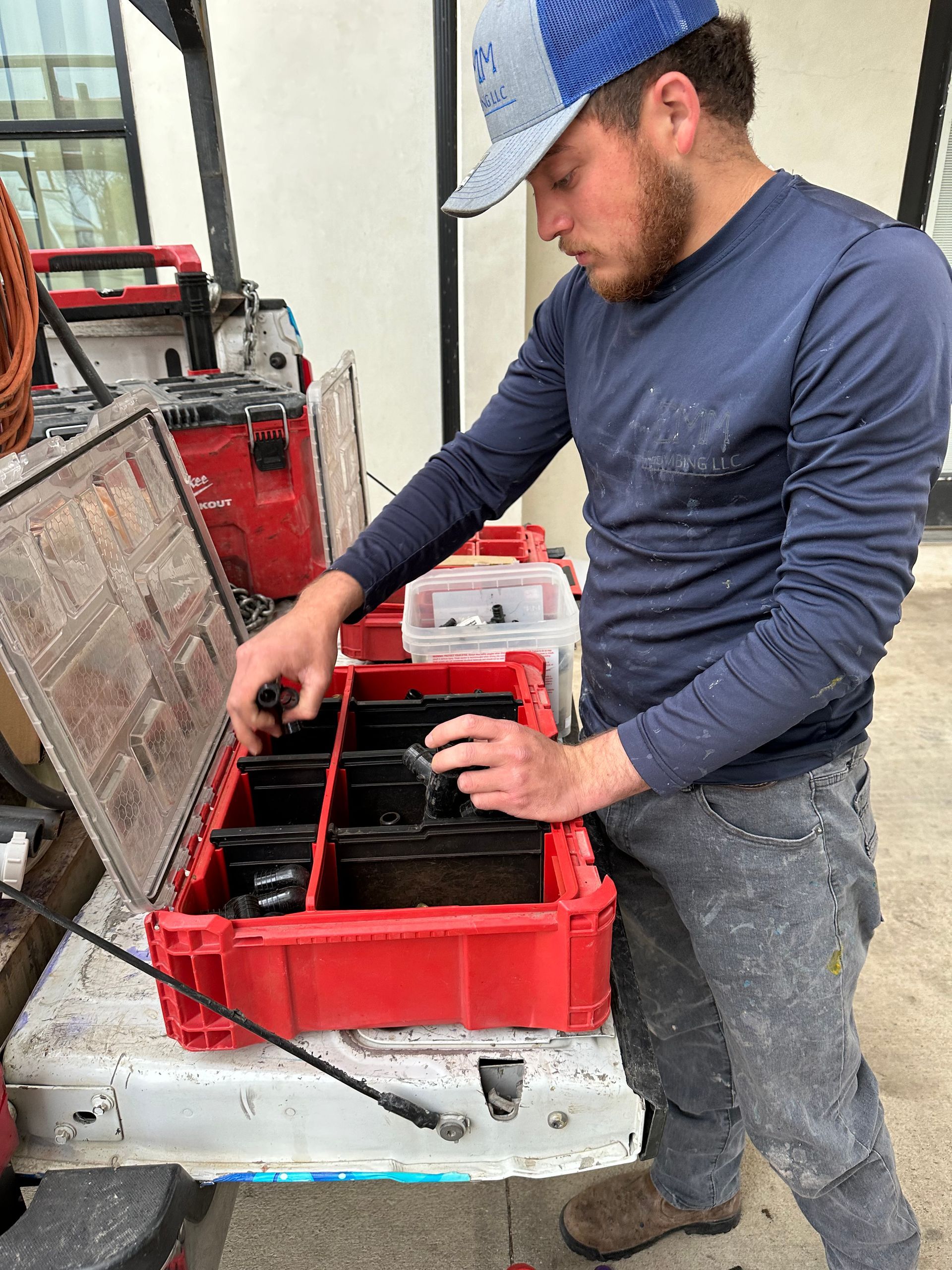 A person in a blue shirt and baseball cap reaching into a red toolbox on a truck bed.