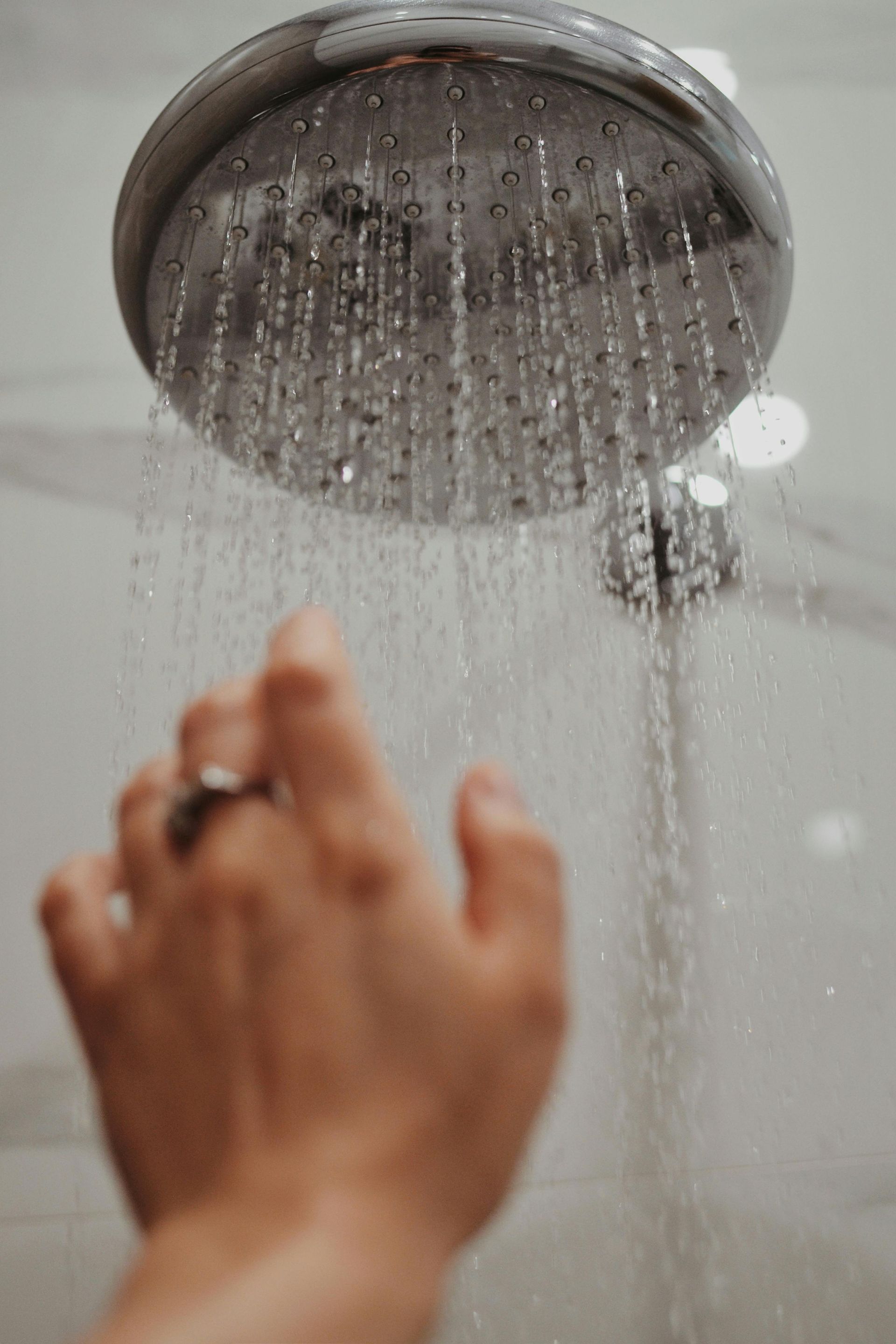 Hand reaching up to turn on a silver showerhead with water streaming down.