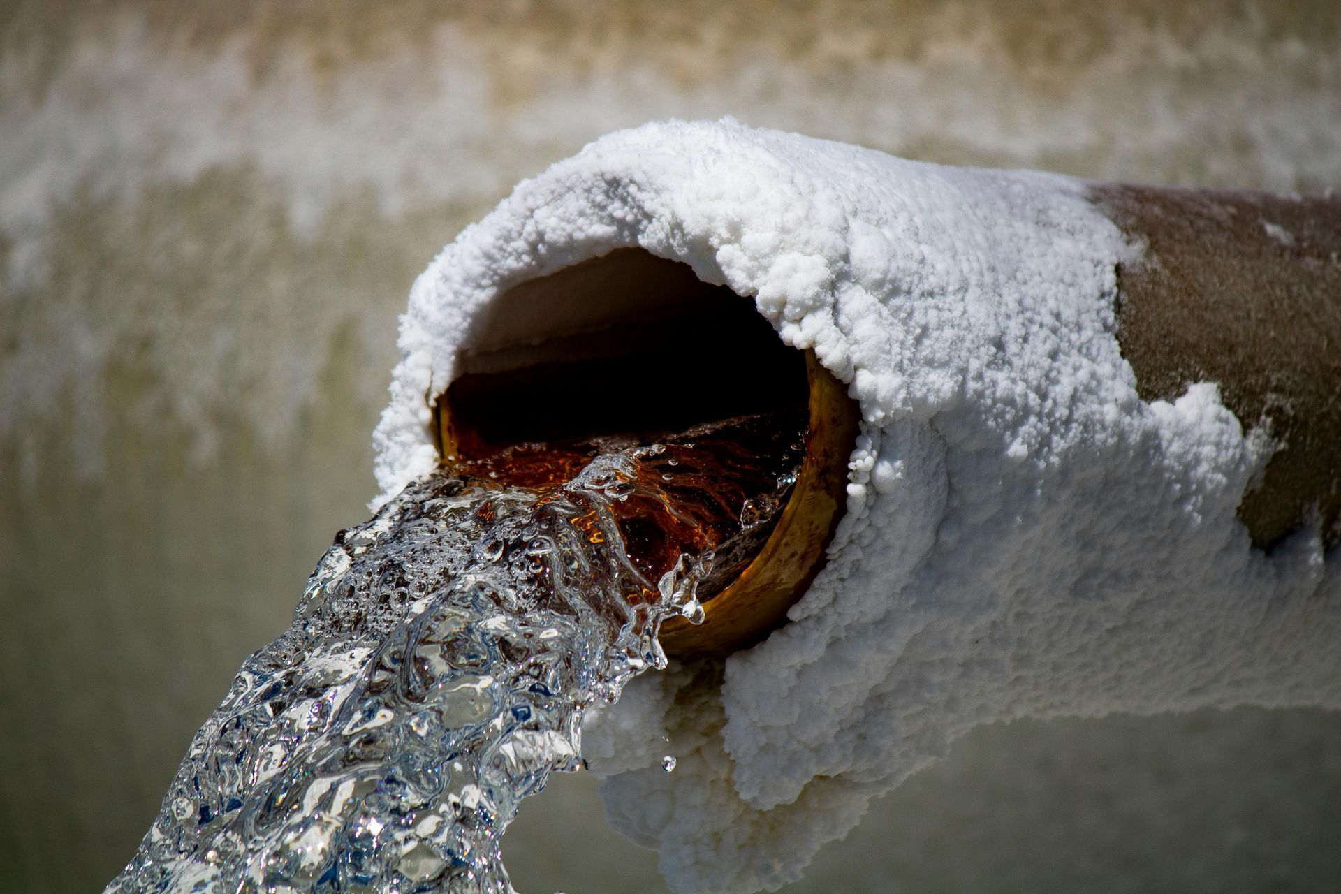 Corroded pipe with water gushing out from an outdoor opening.