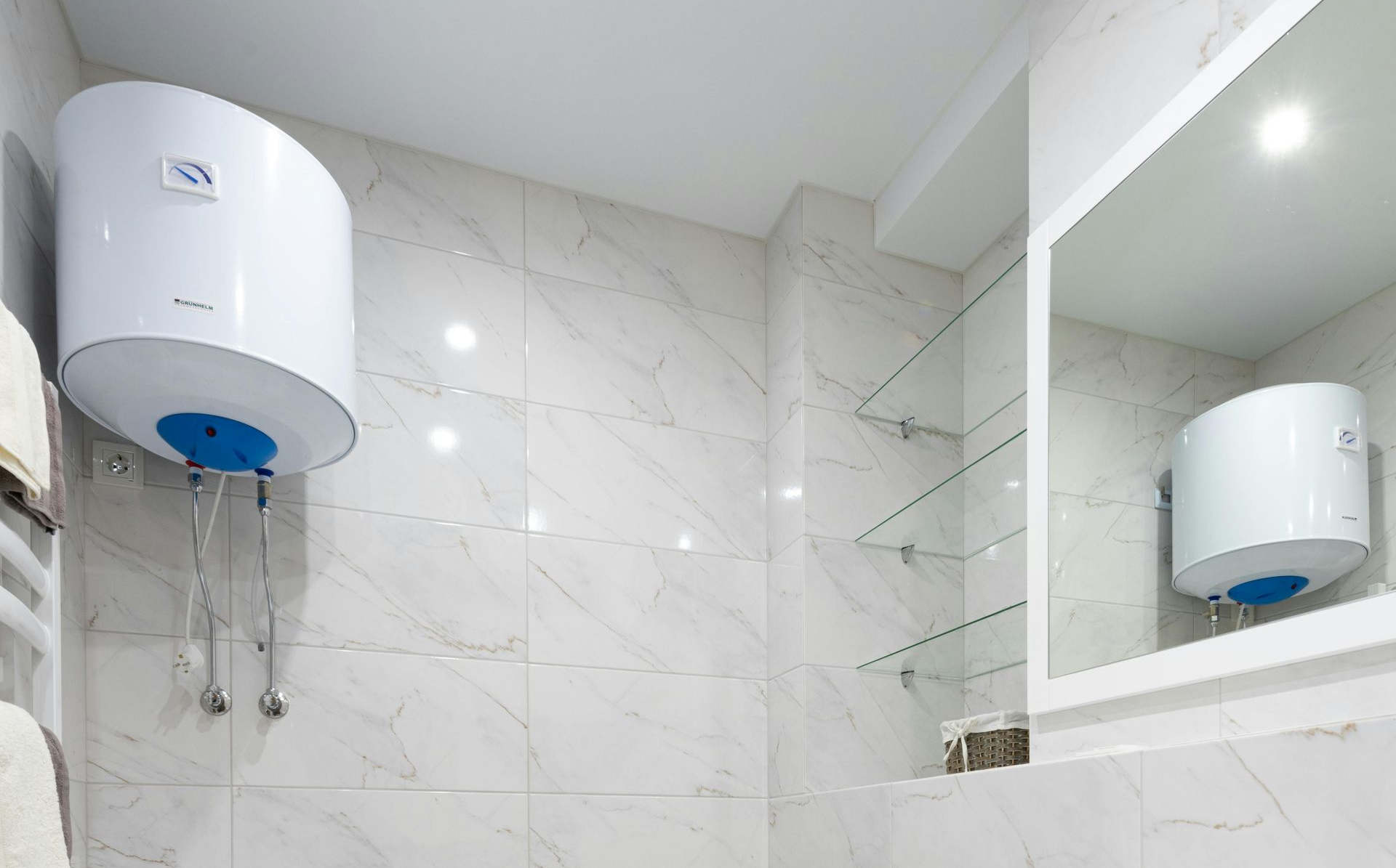 White water heater mounted on white tiled bathroom wall, reflected in a mirror.