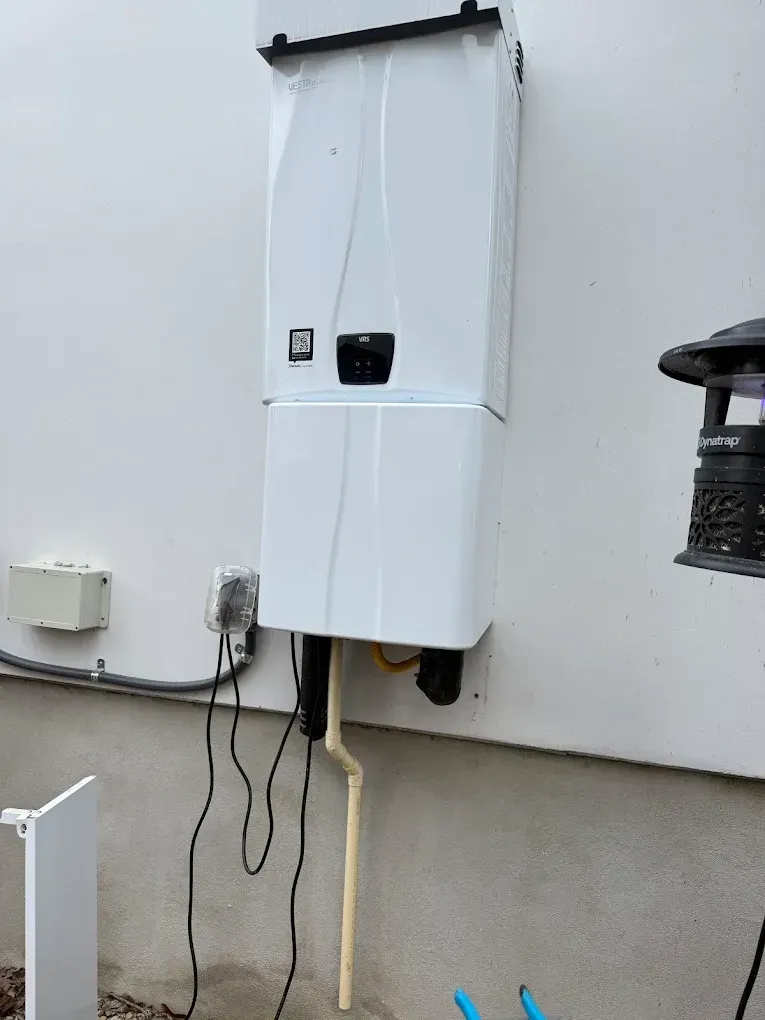 White wall-mounted electrical unit with cables and a small display panel outdoors