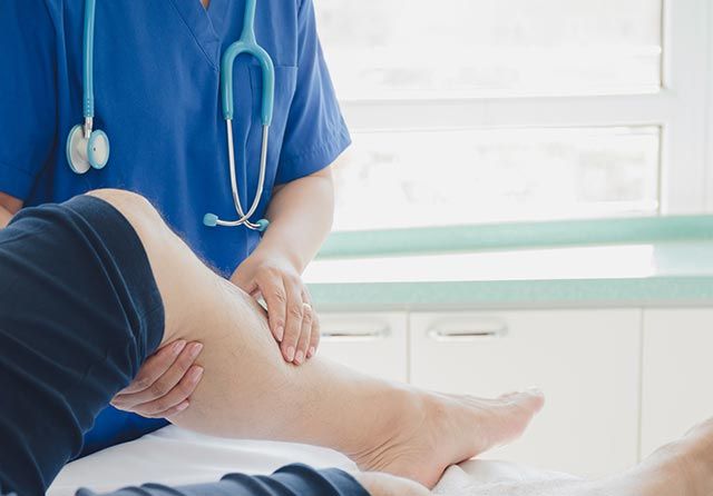 Nurse examining a patient's leg, possibly for injury. Blue scrubs, stethoscope, medical setting.