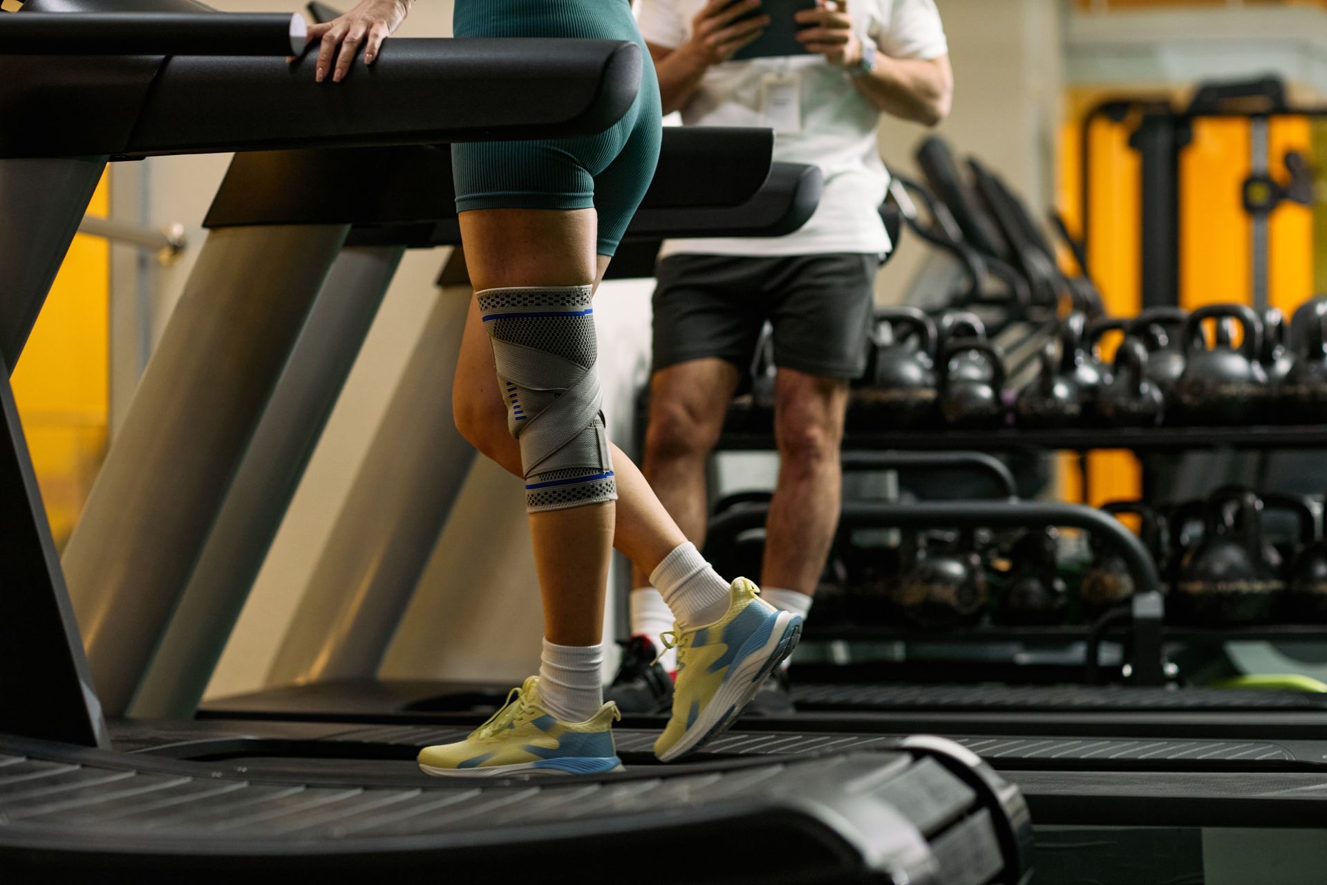 Woman wearing knee brace support walking on treadmill during gym workout rehabilitation.