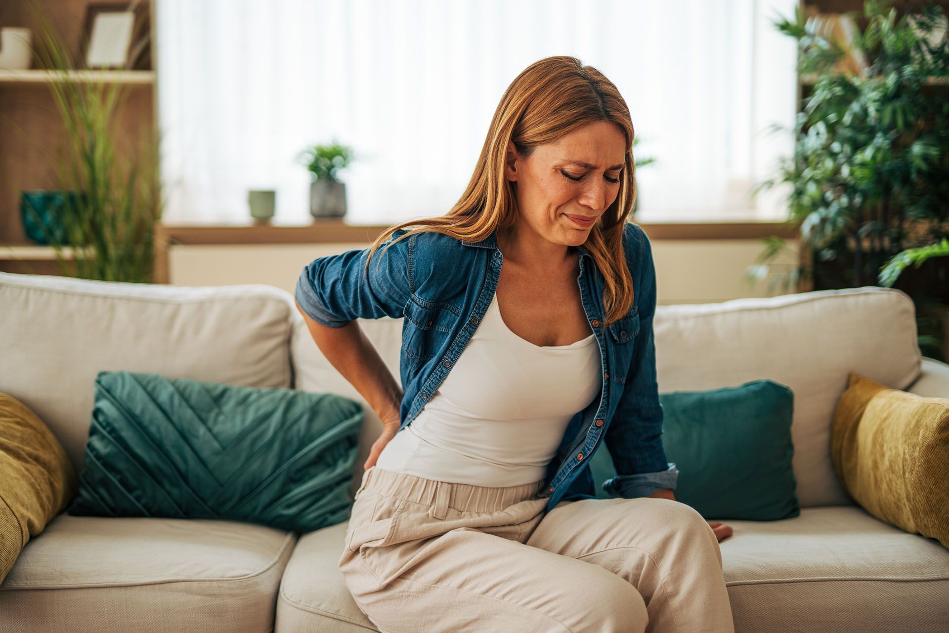 A woman is suffering from back pain while sitting on a sofa. A woman is suffering from back pain while sitting on a sofa.
