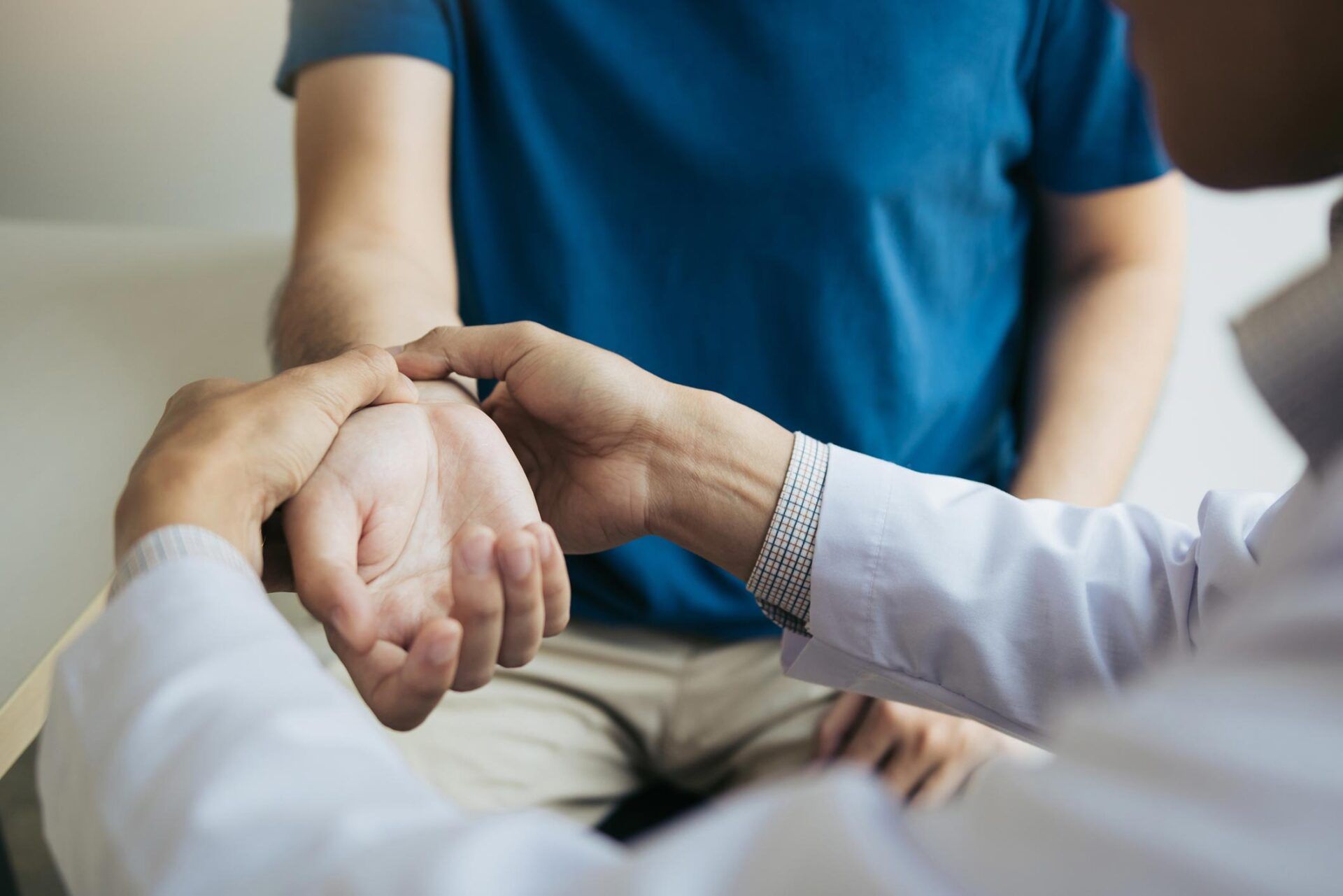 Doctor examining a patient's wrist. The doctor wears a white coat, the patient a blue shirt.