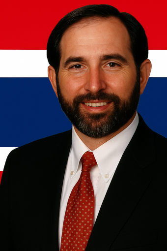 Man with beard in suit, smiling, against background of the flag of Thailand.