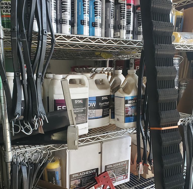 Shelves stocked with cleaning supplies, bottles, paint tubes, leather straps, and tools.
