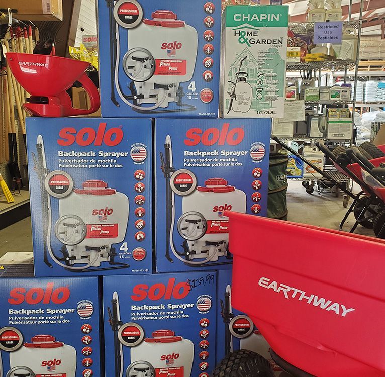 Solo backpack sprayers and Earthway spreader on display in a store. Boxes are blue.