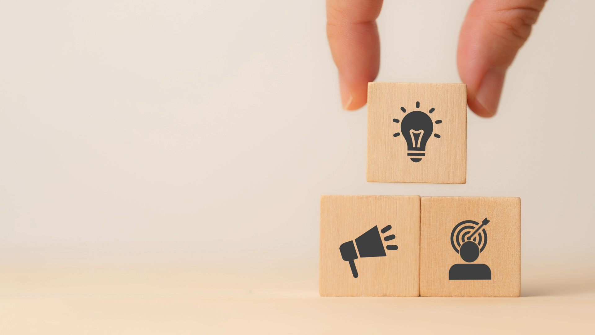 A hand is stacking wooden blocks with icons on them.