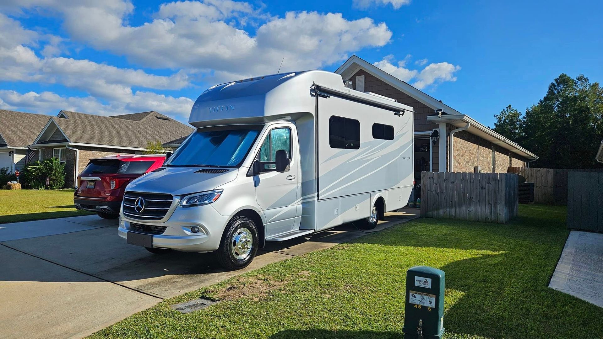 A white rv is parked in a driveway in front of a house.