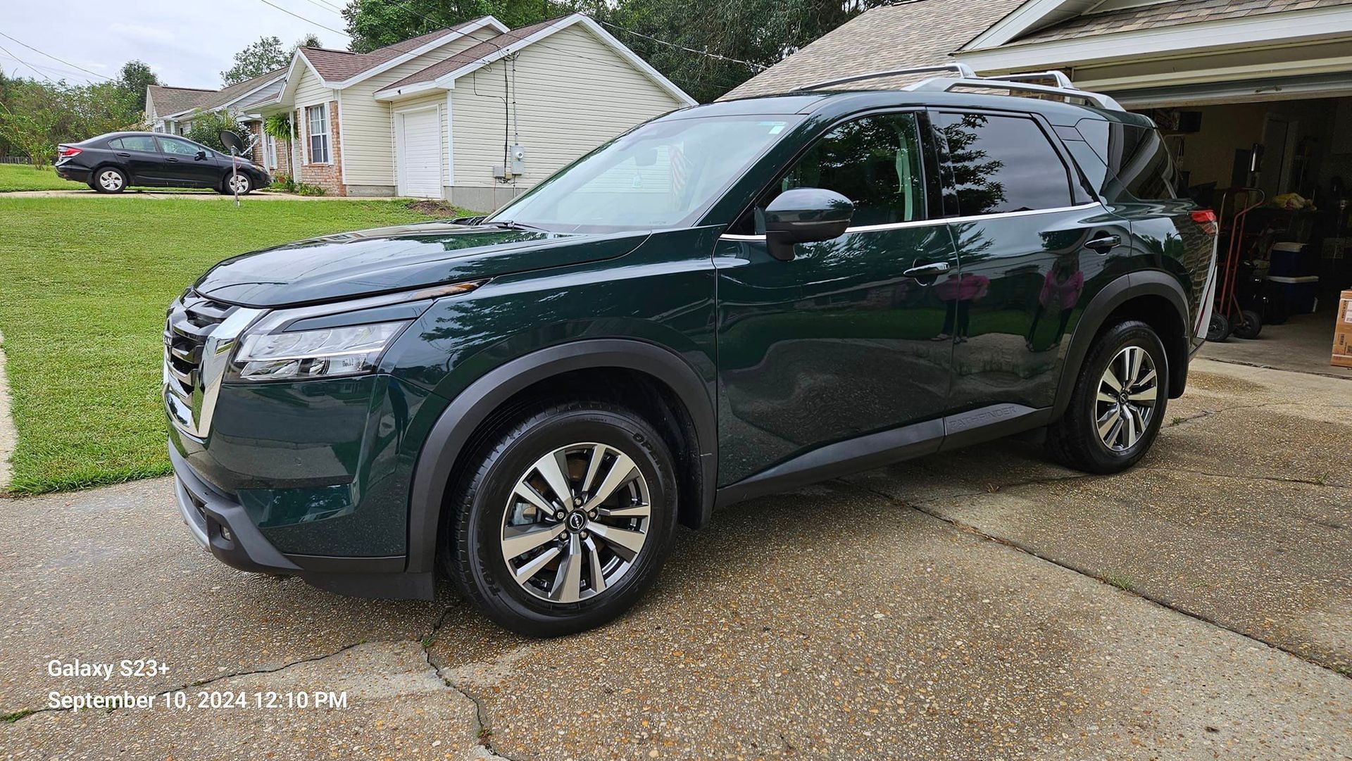 A green nissan pathfinder is parked in front of a garage.