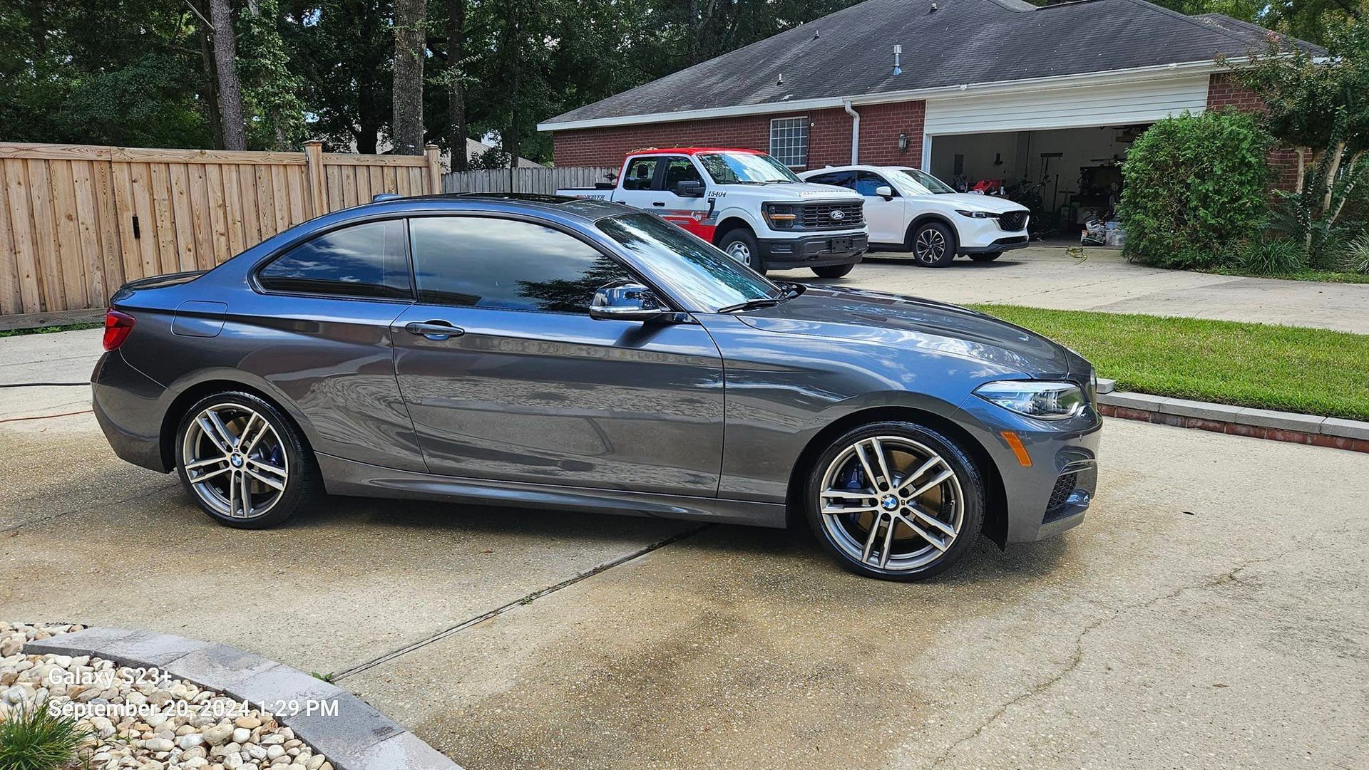 A gray bmw is parked in a driveway in front of a house.