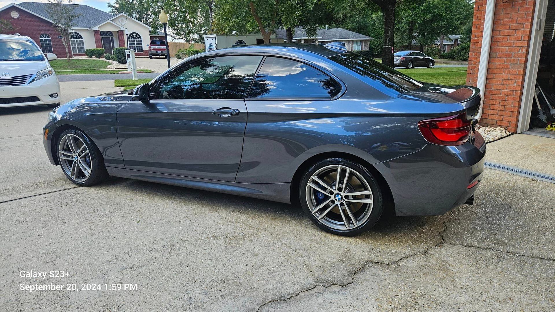 A gray bmw is parked in a driveway next to a garage.