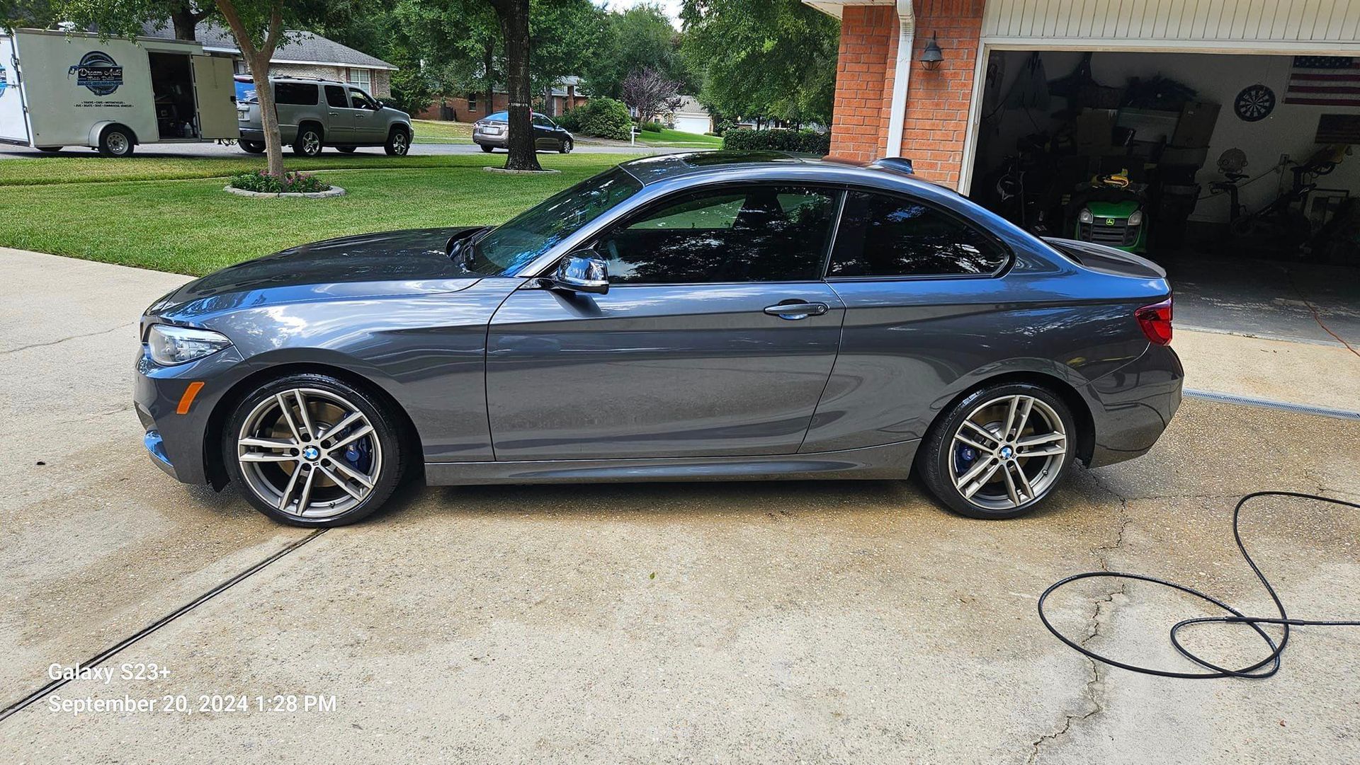 A gray bmw is parked in a driveway next to a garage.