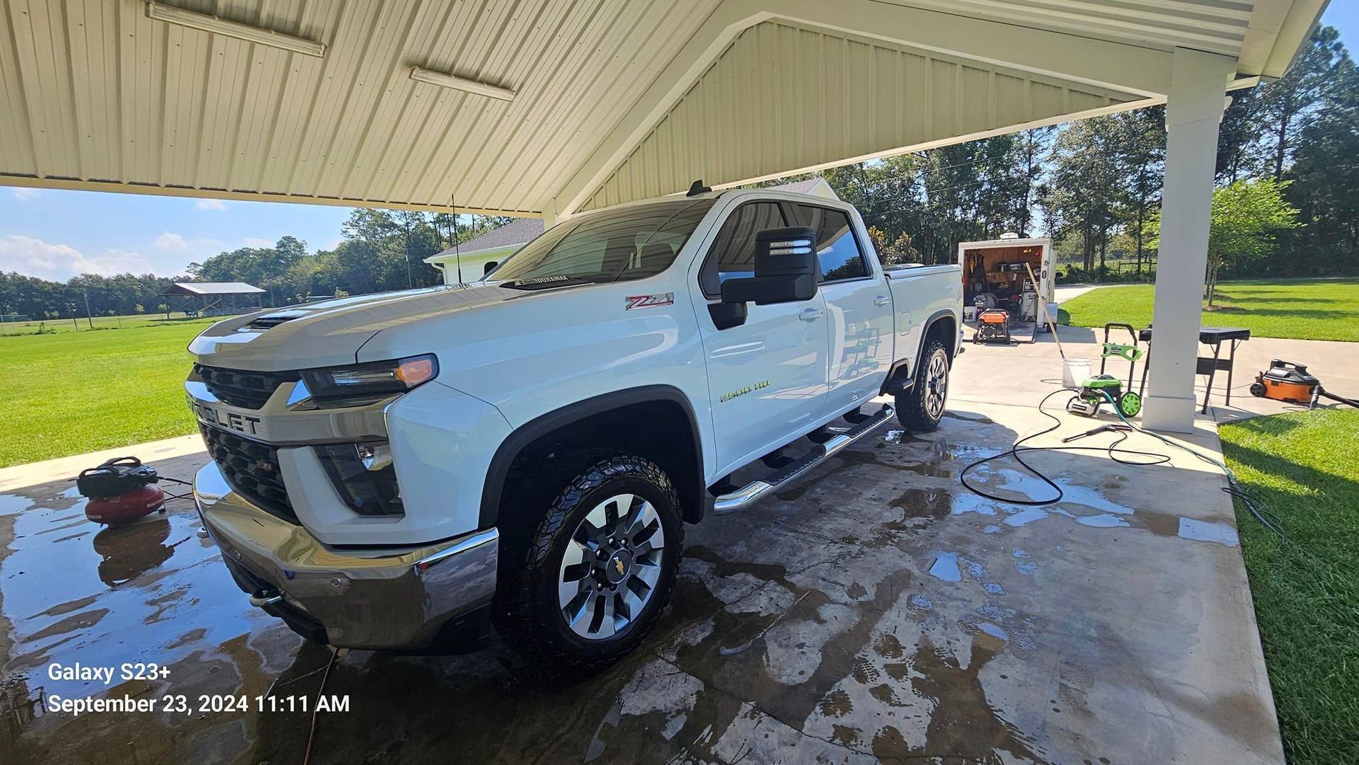 A white truck is parked under a canopy in a driveway.