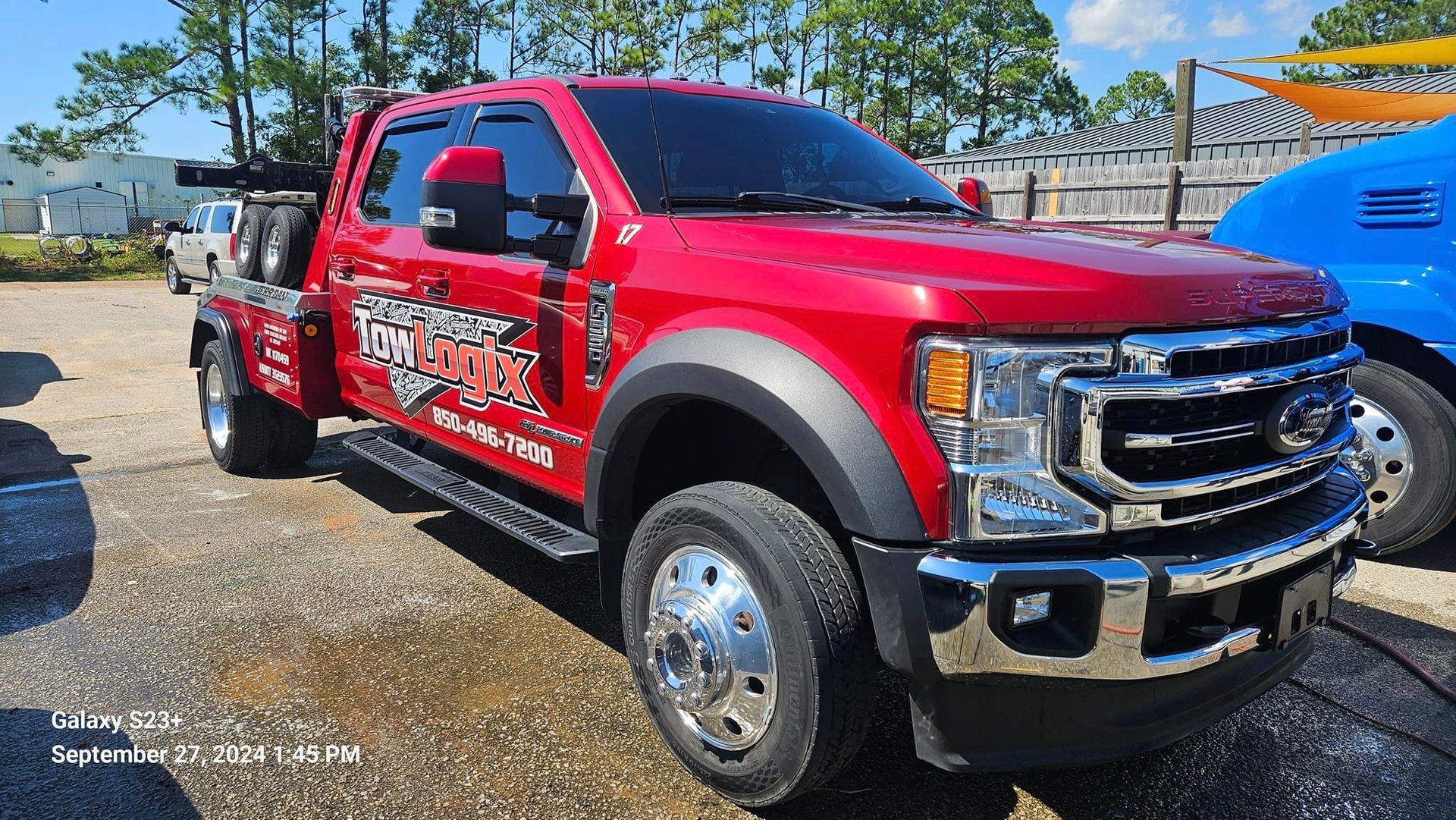 A red tow truck is parked in a parking lot next to a blue truck.