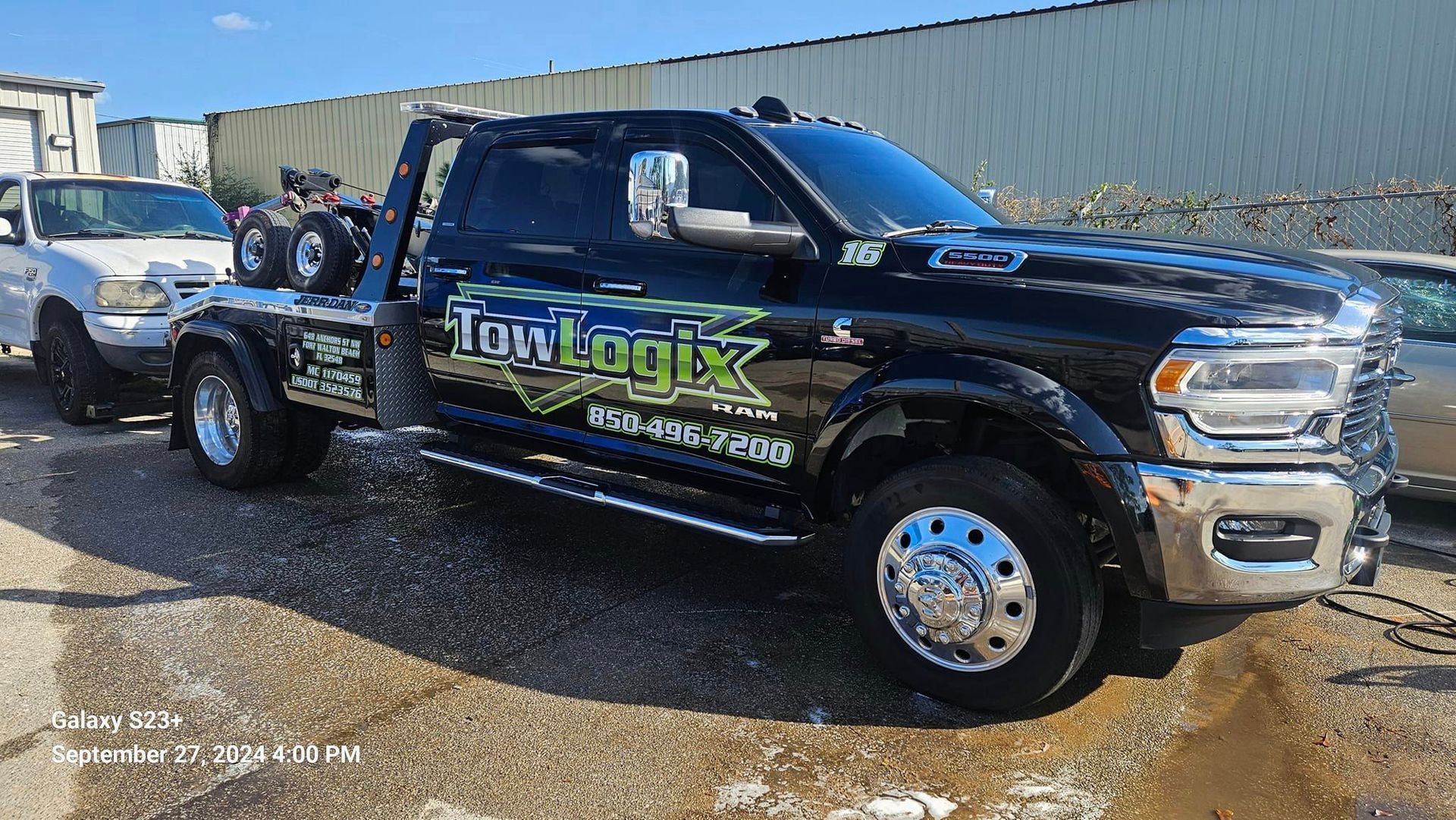 A black tow truck is parked next to a white truck.