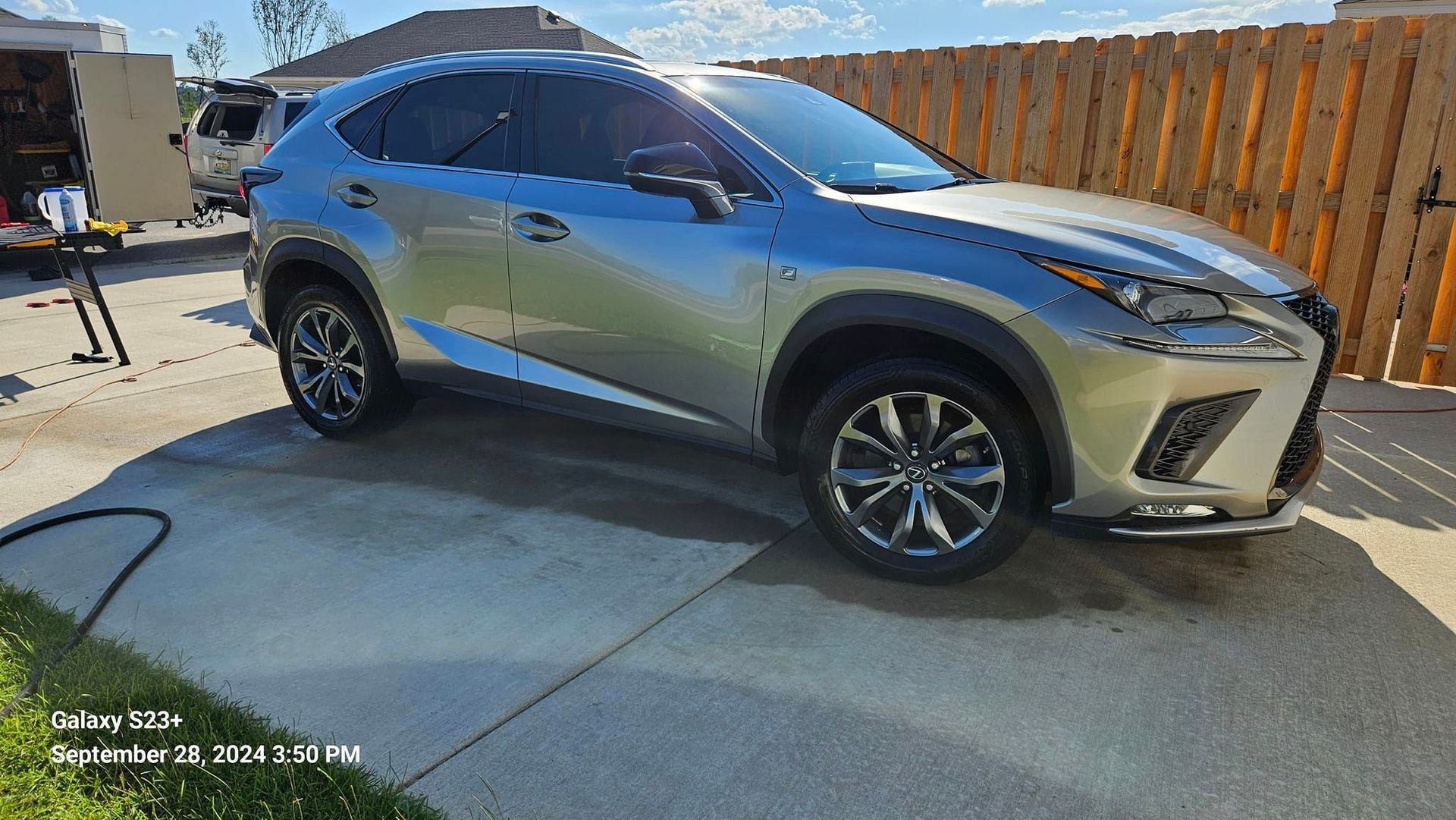 A silver lexus nx is parked in a driveway next to a wooden fence.