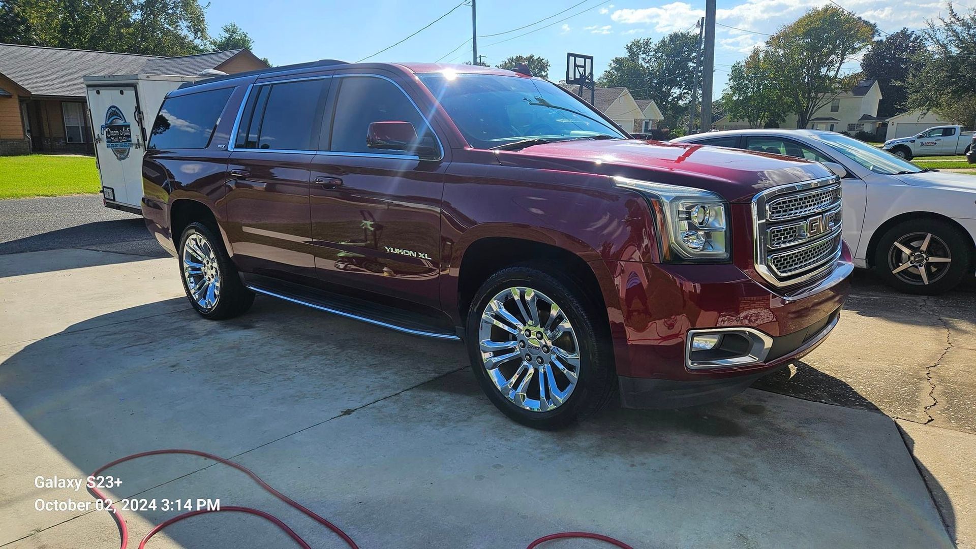 A red gmc yukon is parked in a driveway next to a white car.