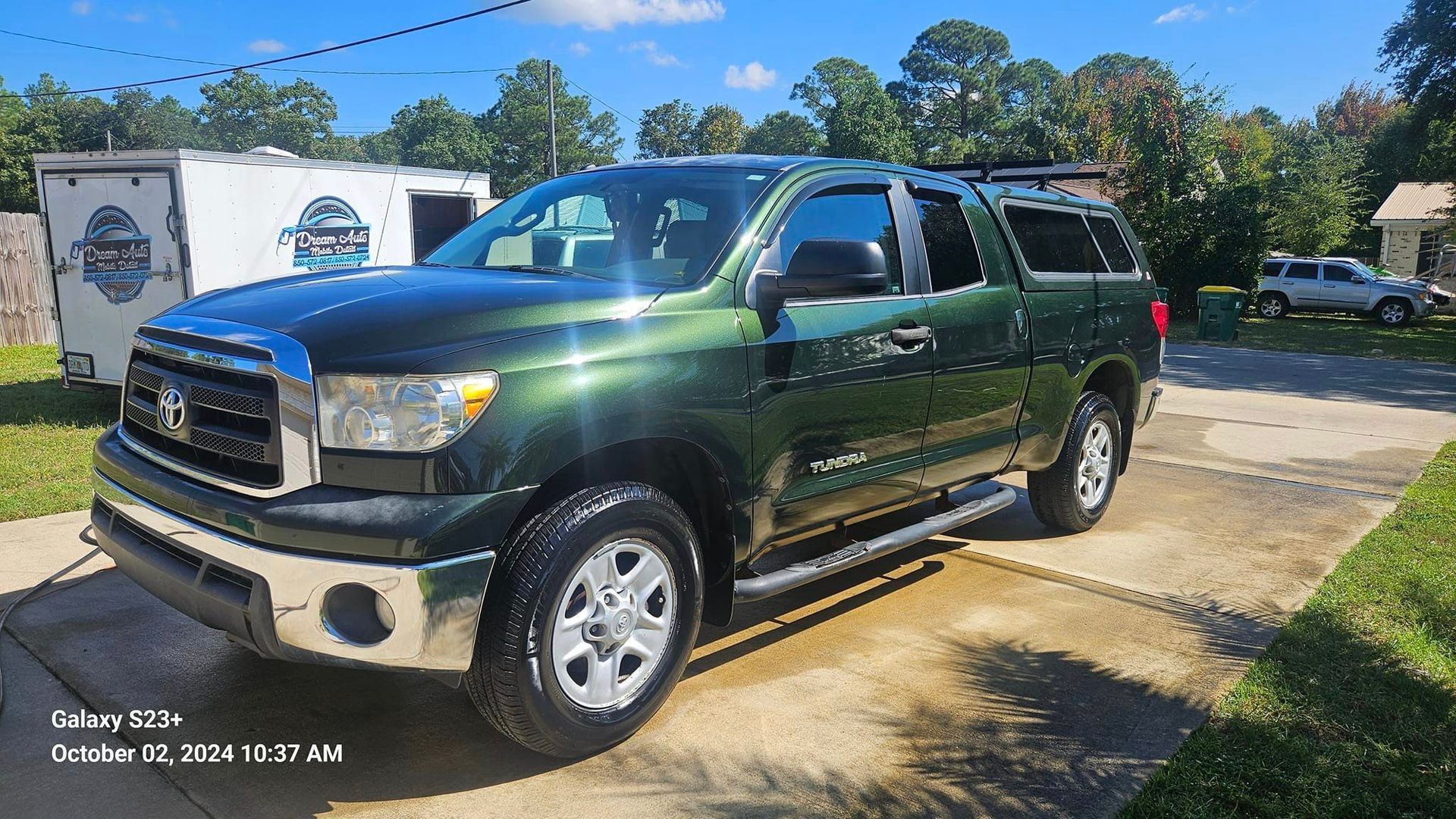 A green toyota tundra is parked in a driveway next to a trailer.