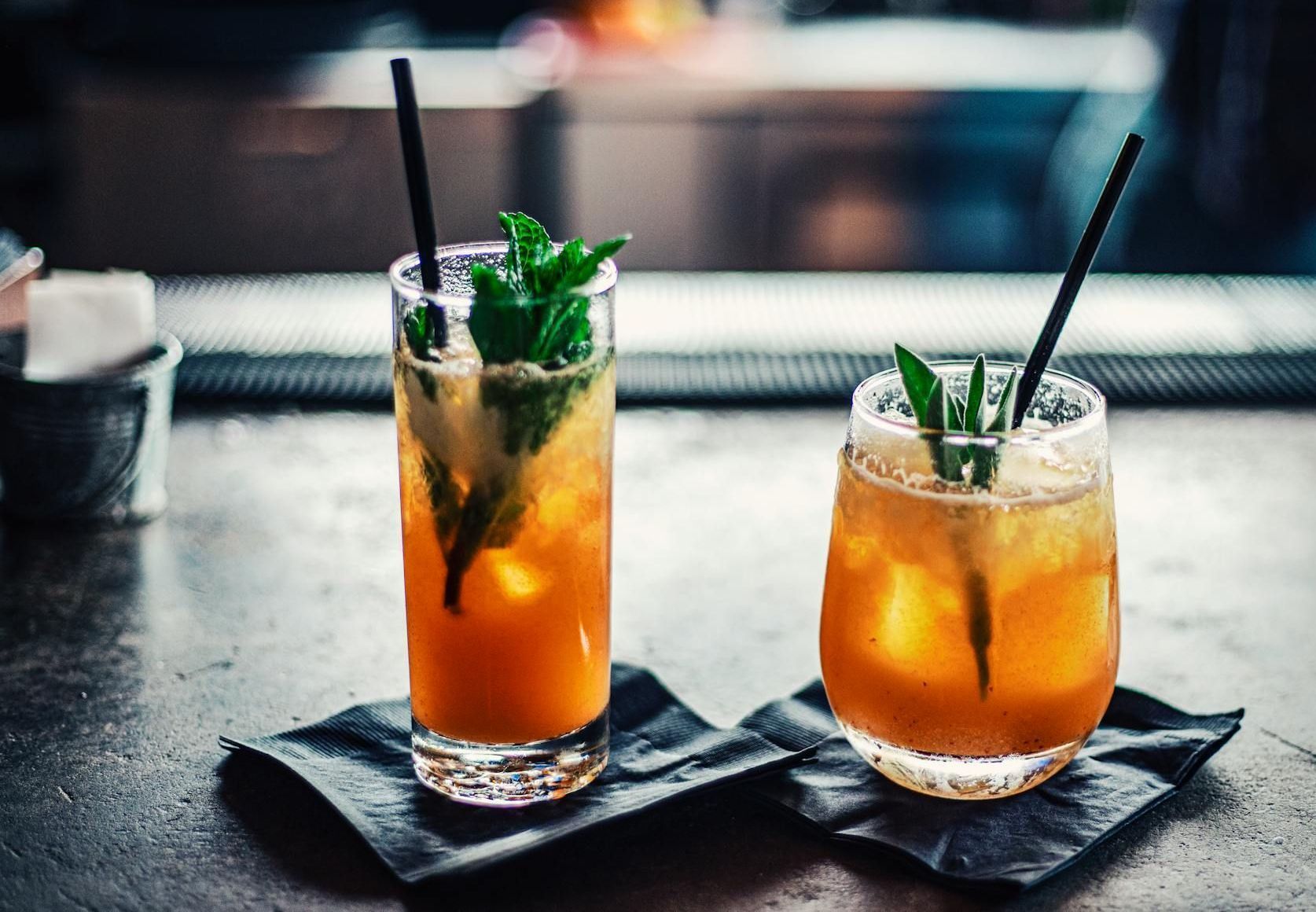 Two glasses of drinks with straws on a table.