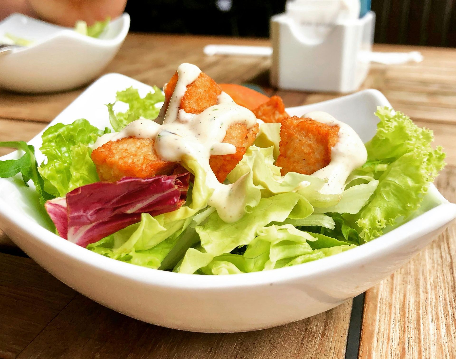 A bowl of salad with lettuce and chicken on a table