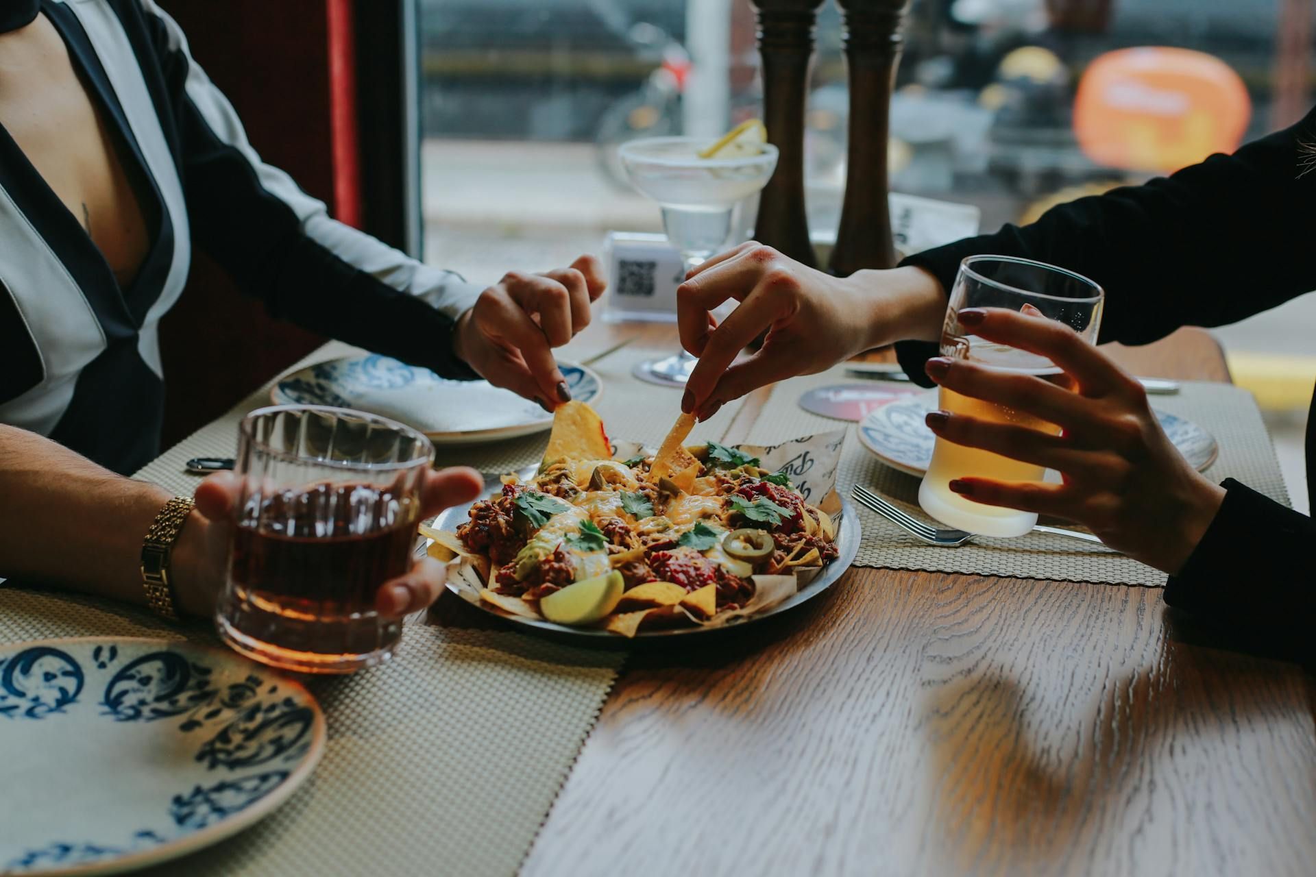 Two people are sitting at a table eating nachos and drinking beer.