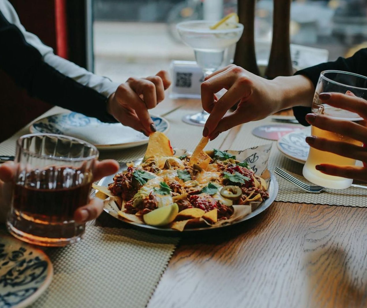 Two people are sitting at a table eating nachos and drinking beer