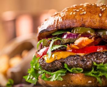 A close up of a hamburger with lettuce , cheese , onions and peppers.