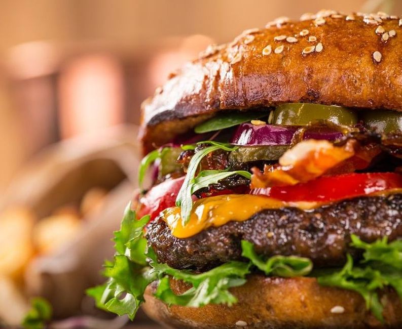 A close up of a hamburger with lettuce , cheese , onions and peppers.