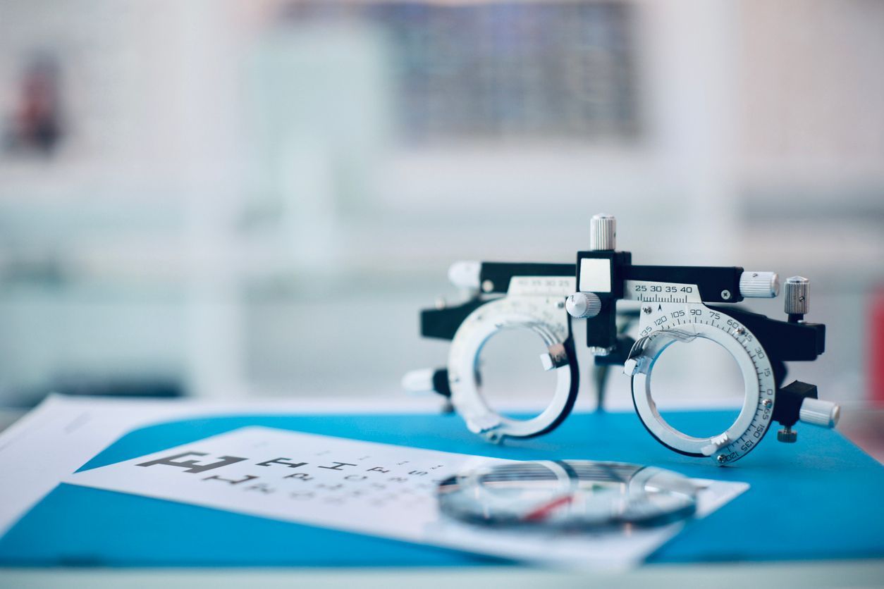 Optometry tools on a blue surface: a phoropter and eyeglass lenses.