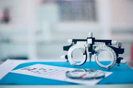 Optometry tools on a blue surface: a phoropter and eyeglass lenses.