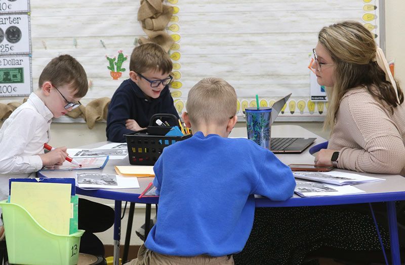 A teacher assists three students at a table in a classroom. The Immanuel Difference | Immanuel Lutheran School | Belvidere, IL